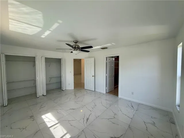 Spacious room featuring large format white tile flooring with gray veining, dual bi-fold door closets, a ceiling fan with integrated lighting, and multiple entryways