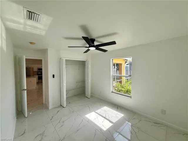 Spacious room featuring large format tile flooring, a window with exterior visibility, a ceiling fan with integrated lighting, and a bi-fold closet