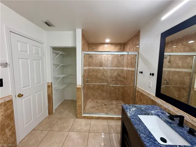 Bathroom featuring a tiled shower with glass enclosure, a vanity with a blue granite countertop and undermount sink, and tiled flooring