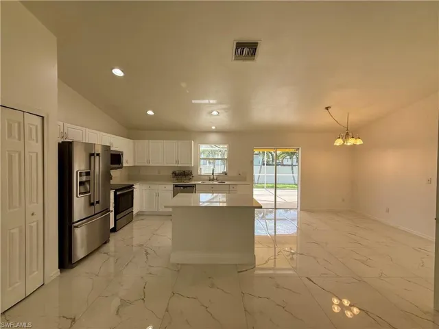 Open-concept kitchen and living area featuring white cabinetry, stainless steel appliances, a center island, vaulted ceilings, and large format tile flooring