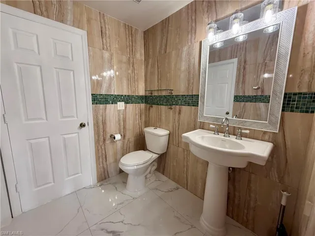 Bathroom featuring floor-to-ceiling stone-look tile, a green mosaic tile accent band, and white porcelain pedestal sink