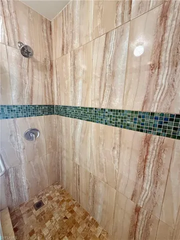 Shower featuring vertical-format stone-look wall tiles, a mosaic tile accent band, a square-tile shower floor, and a chrome showerhead with matching controls