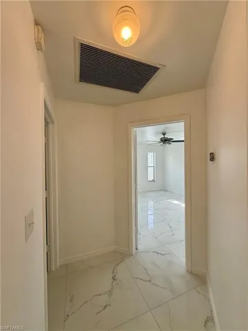Hallway featuring white tile flooring with gray veining and bright white walls