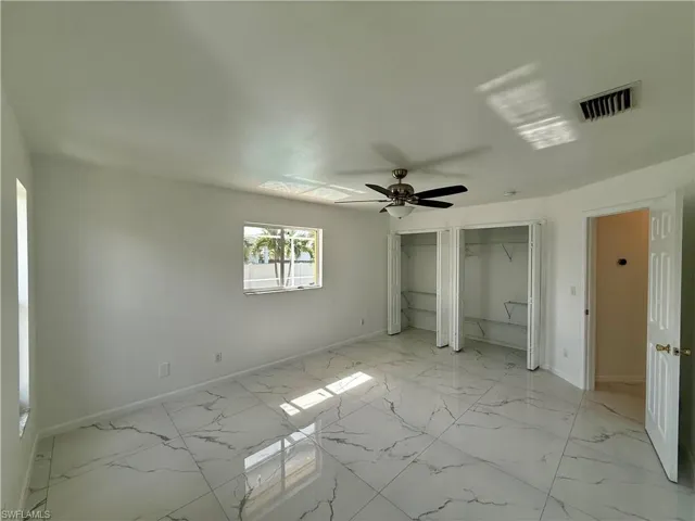 Spacious interior featuring white walls, large format tile flooring with veining, and a ceiling fan with integrated lighting