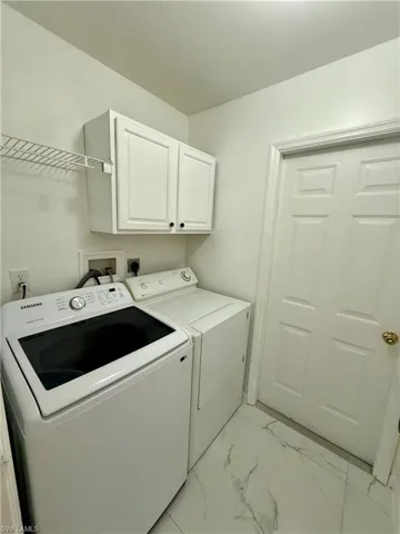 Dedicated laundry area featuring white upper cabinetry, wire shelving, and light-toned flooring with subtle veining