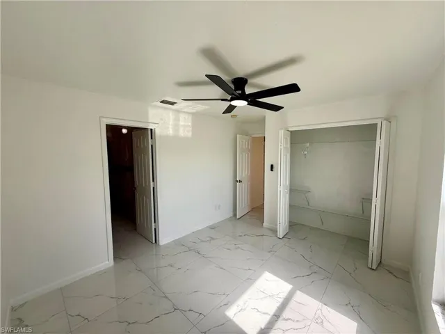 Spacious room featuring large format white tile flooring with gray veining, a ceiling fan with integrated lighting, a double-door closet with shelving, and crisp white walls