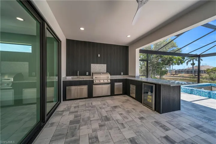 View of patio featuring a sink, grilling area, exterior kitchen, an in ground hot tub, and a lanai