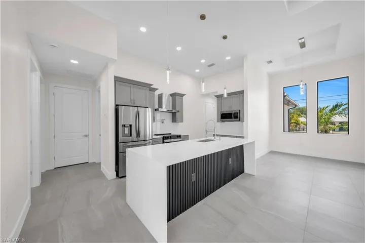 Kitchen with baseboards, gray cabinets, wall chimney exhaust hood, a sink, and stainless steel appliances