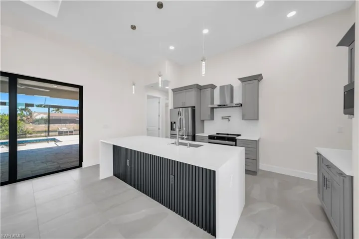 Kitchen featuring baseboards, light countertops, wall chimney exhaust hood, gray cabinetry, and stainless steel appliances