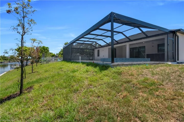 Back of property featuring a water view, glass enclosure, and a yard