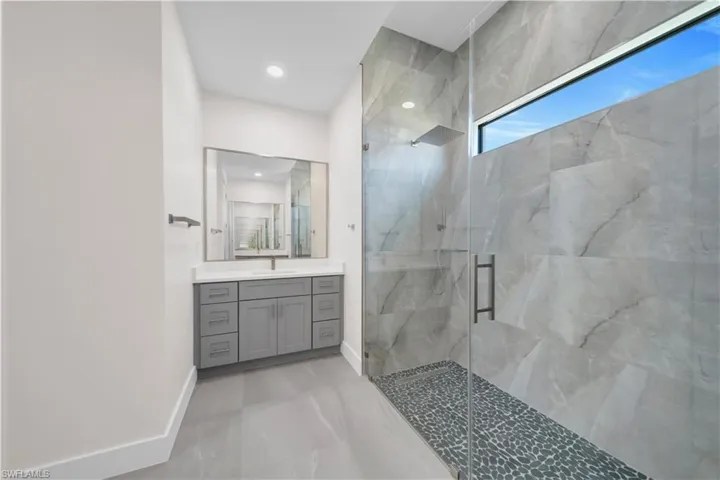 Full bath featuring baseboards, a marble finish shower, marble finish floor, and vanity