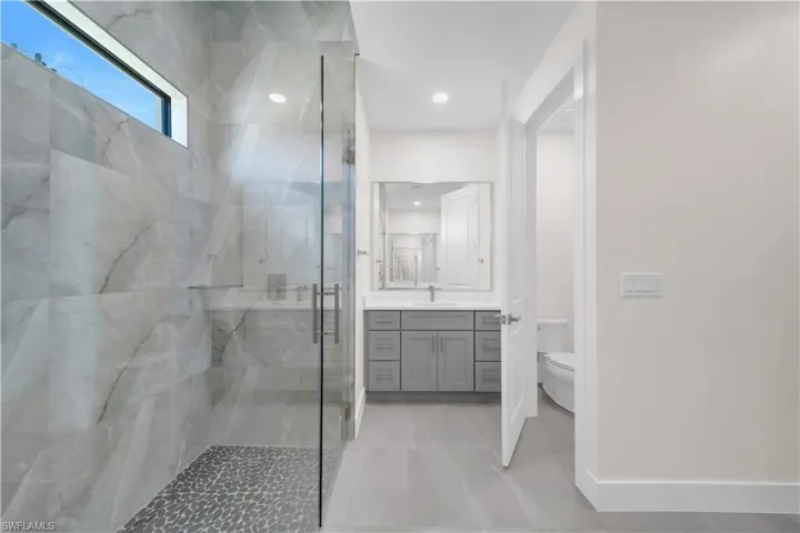 Full bathroom with vanity, toilet, a marble finish shower, recessed lighting, and baseboards