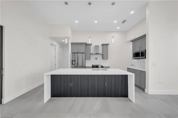 Kitchen with baseboards, appliances with stainless steel finishes, a center island with sink, and gray cabinets