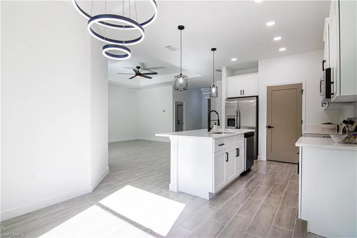 Kitchen featuring white cabinetry, sink, light hardwood / wood-style flooring, an island with sink, and ceiling fan with notable chandelier