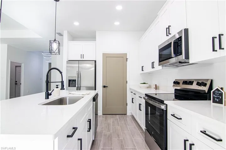 Kitchen with a center island with sink, white cabinets, sink, hanging light fixtures, and stainless steel appliances