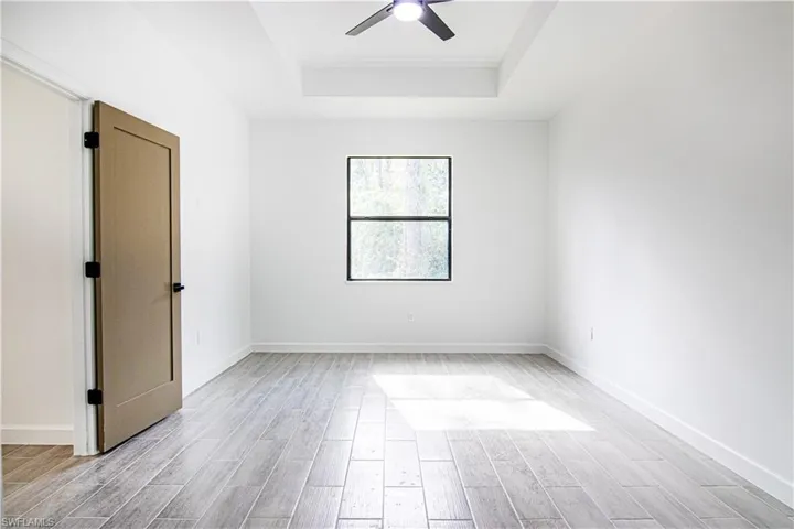 Empty room with a raised ceiling, ceiling fan, and light wood-type flooring