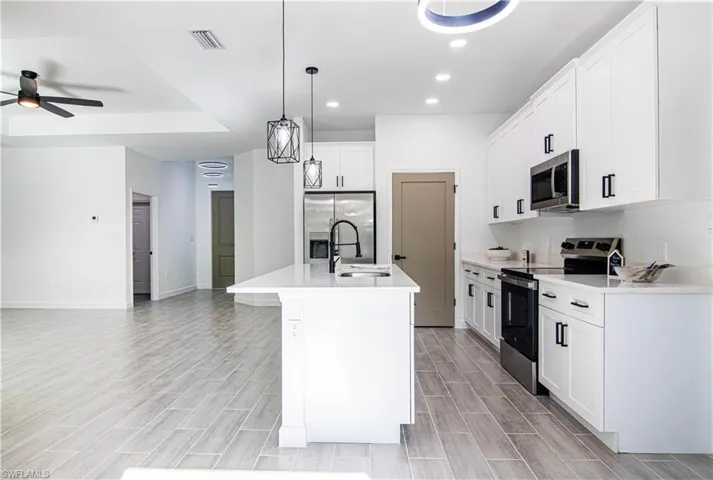 Kitchen featuring appliances with stainless steel finishes, a kitchen island with sink, light hardwood / wood-style flooring, white cabinetry, and hanging light fixtures