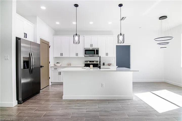 Kitchen with pendant lighting, white cabinets, stainless steel appliances, and a center island with sink