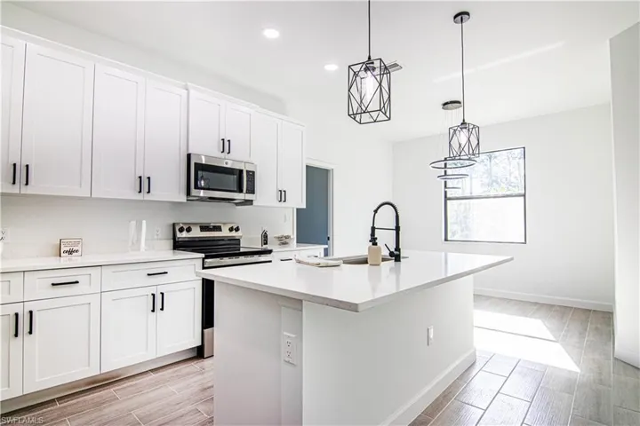 Kitchen with white cabinetry, light hardwood / wood-style flooring, an island with sink, and stainless steel appliances