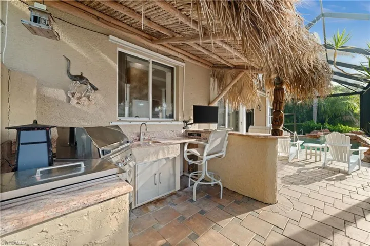 View of patio featuring exterior kitchen, a sunroom, and glass enclosure