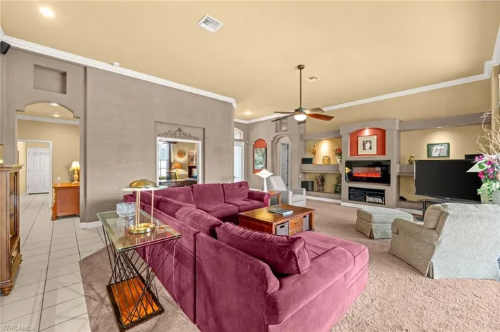 Living room featuring crown molding, arched walkways, a fireplace, ceiling fan, and light tile patterned floors