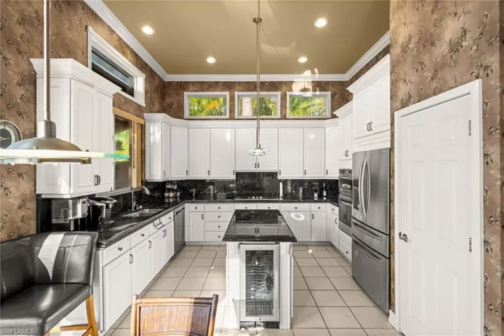 Kitchen with wallpapered walls, dark stone counters, ornamental molding, pendant lighting, and beverage cooler