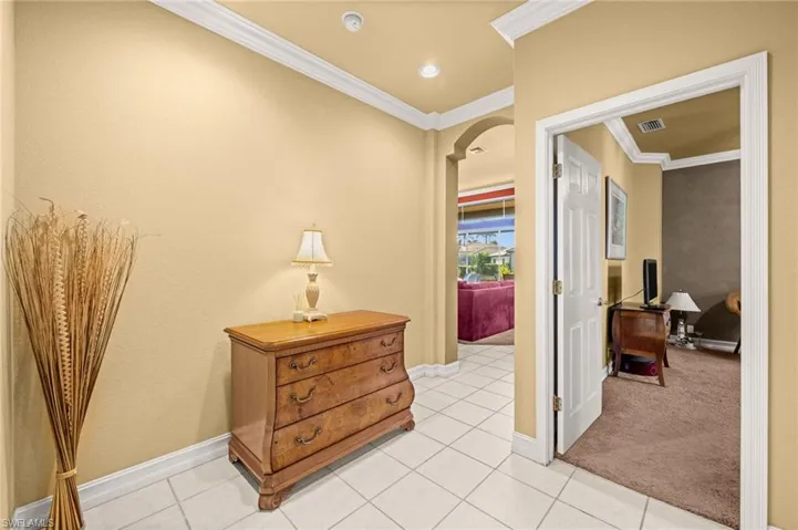 Hallway featuring arched walkways, light colored carpet, crown molding, and light tile patterned floors