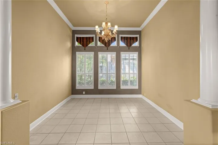 Unfurnished room with decorative columns, ornamental molding, light tile patterned flooring, and a chandelier