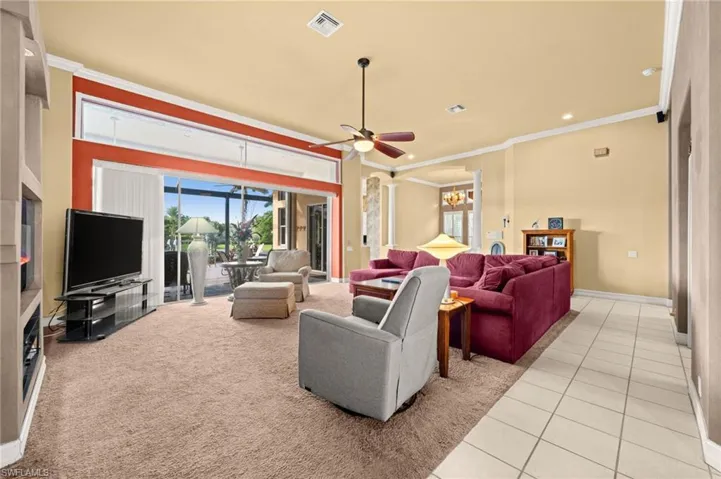 Living room featuring crown molding, healthy amount of natural light, light tile patterned flooring, ceiling fan, and a chandelier