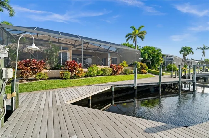 Dock featuring a lanai, a sunroom, boat lift, a water view, and a yard