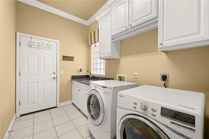 Laundry area featuring ornamental molding, light tile patterned flooring, washer and dryer, and cabinet space