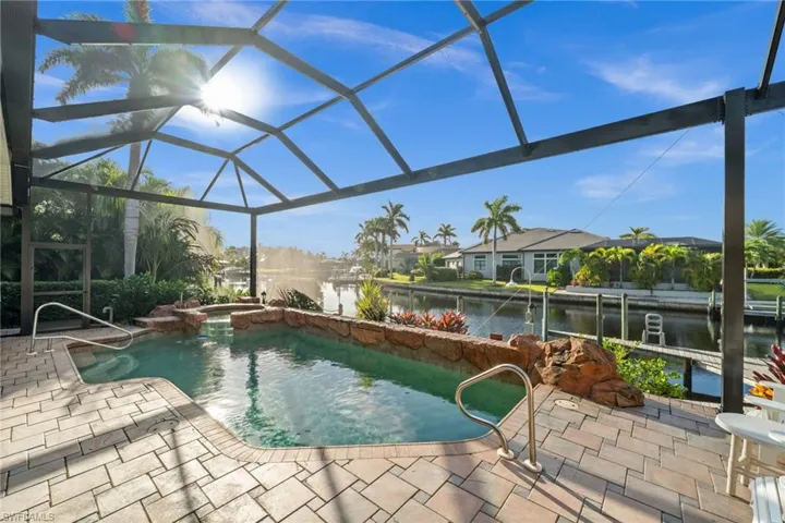 View of swimming pool with a lanai, a sunroom, a water view, a pool with connected hot tub, and a patio area