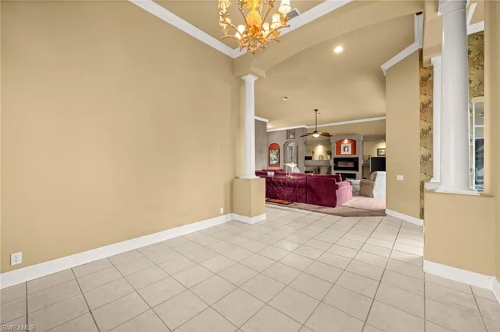 Unfurnished room with decorative columns, light tile patterned floors, a fireplace, crown molding, and recessed lighting