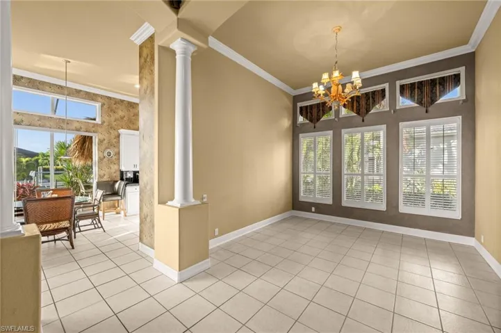 Unfurnished room featuring ornate columns, a chandelier, crown molding, plenty of natural light, and light tile patterned flooring