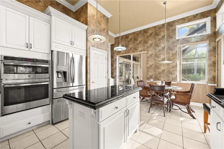 Kitchen featuring white cabinets, pendant lighting, appliances with stainless steel finishes, ornamental molding, and a center island