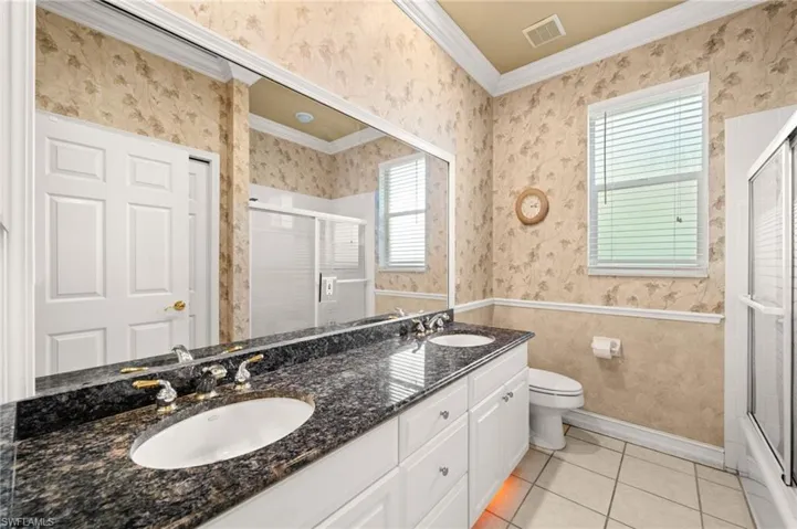 Bathroom featuring wallpapered walls, plenty of natural light, light tile patterned floors, double vanity, and crown molding