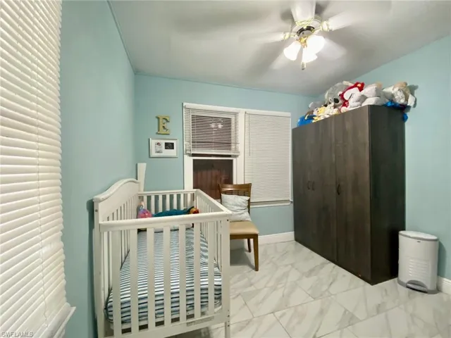 Bedroom with light tile patterned floors, a nursery area, and ceiling fan