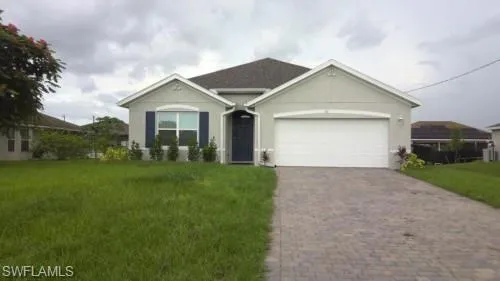 Ranch-style house featuring a front yard, an attached garage, stucco siding, and decorative driveway