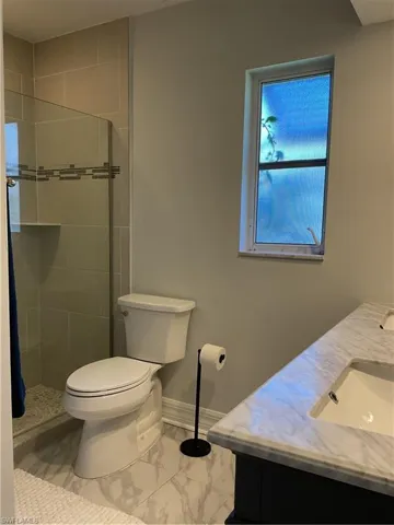 Full bath with double vanity, marble finish floors, and a stall shower