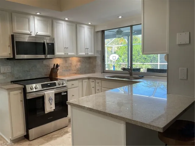 Kitchen with range, white microwave, a peninsula, a breakfast bar area, and light stone countertops