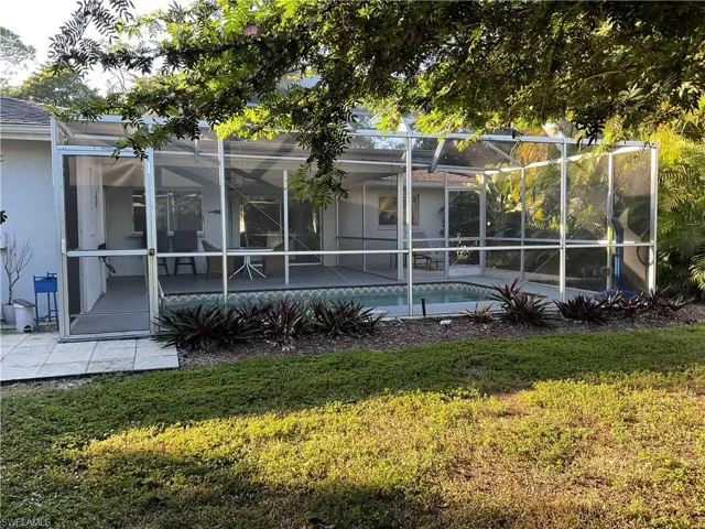 Back of house featuring an outdoor pool, a sunroom, glass enclosure, a lawn, and stucco siding