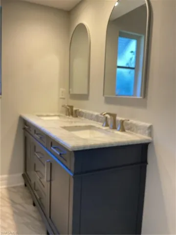 Full bath featuring double vanity and light marble finish floors