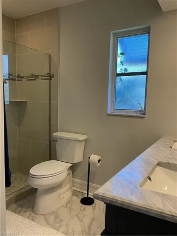 Bathroom with double vanity, marble look tiles, and a stall shower