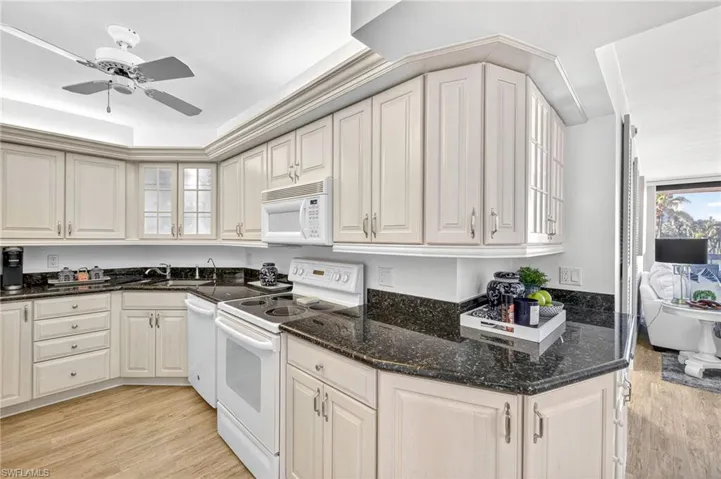 Kitchen featuring white appliances, light wood-type flooring, a ceiling fan, and dark stone countertops