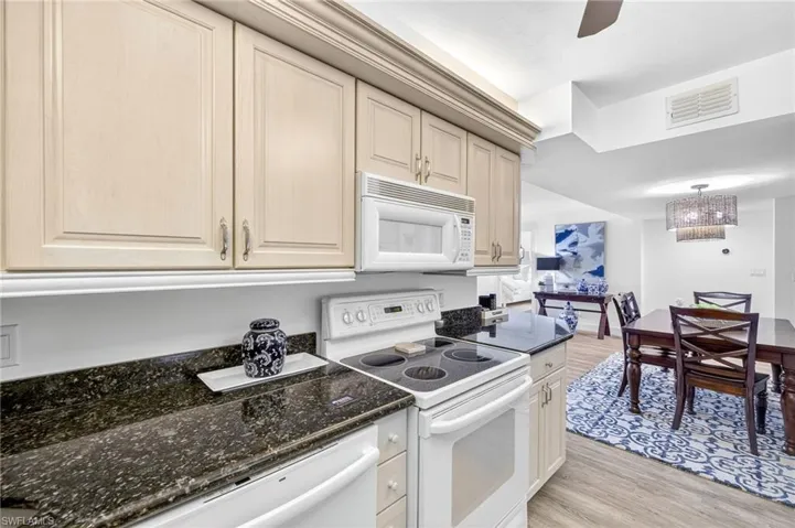 Kitchen featuring white appliances, light wood-style floors, a chandelier, dark stone counters, and a ceiling fan