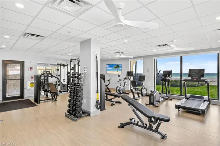 Exercise room with a ceiling fan, healthy amount of natural light, a drop ceiling, wood finished floors, and recessed lighting