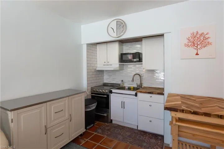 Compact kitchen area featuring white cabinetry, a subway tile backsplash, and a stainless steel sink with a gooseneck faucet