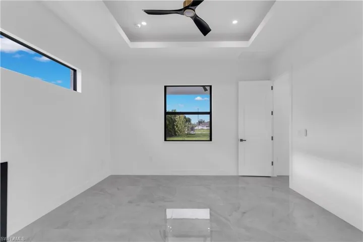 Empty room featuring ceiling fan, a wealth of natural light, and a raised ceiling
