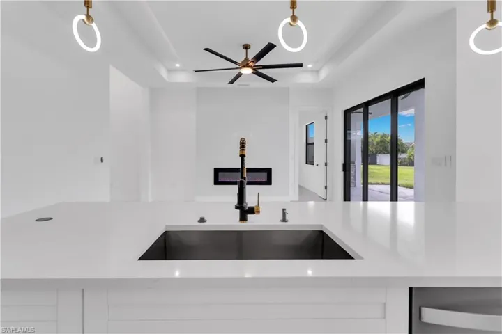 Kitchen with a raised ceiling, ceiling fan, sink, and light stone countertops