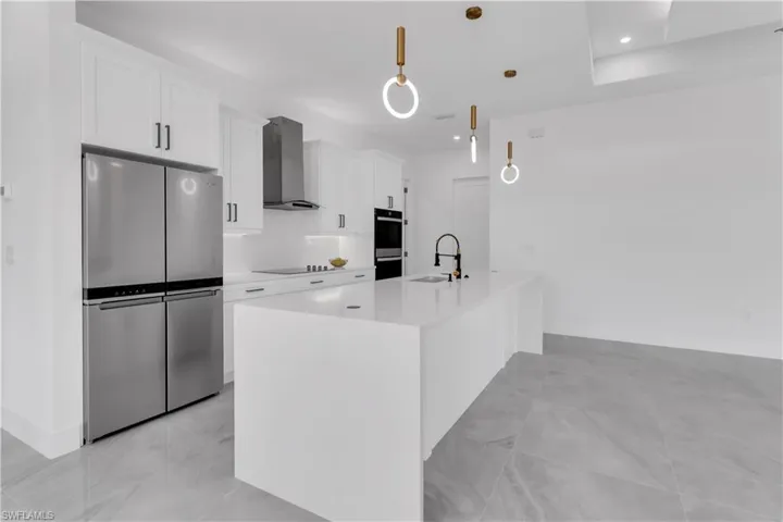 Kitchen with a center island with sink, pendant lighting, stainless steel appliances, white cabinetry, and wall chimney range hood